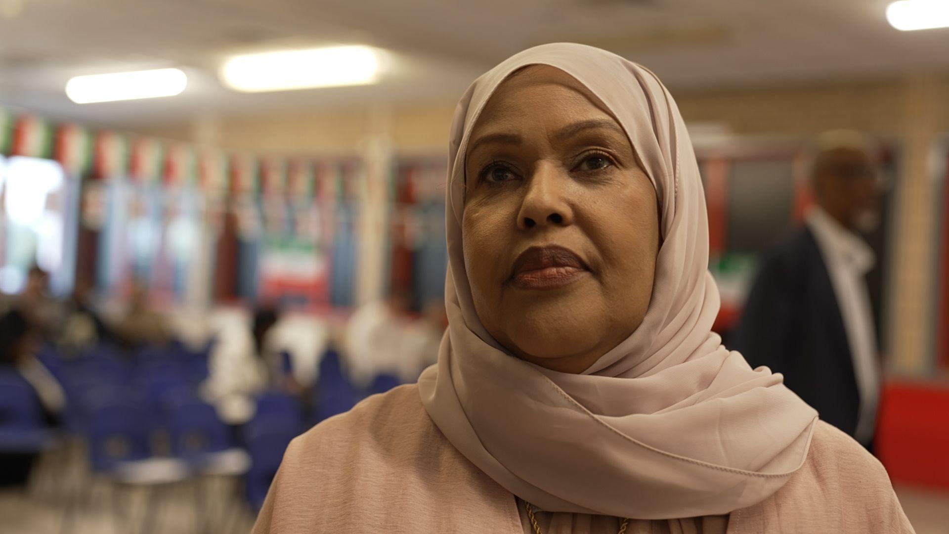Fatima looks at the camera in a conference room. She's wearing a light pink head scarf and Abaya dress.