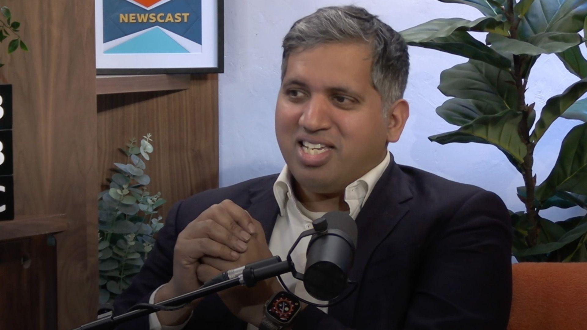 Faisal Islam wearing a suit sitting behind a microphone in the Newscast studio