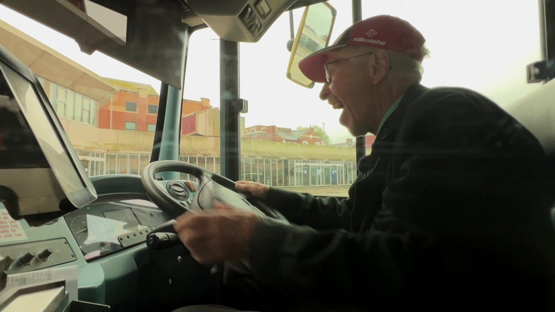 Norman, smiling, at the wheel of a bus