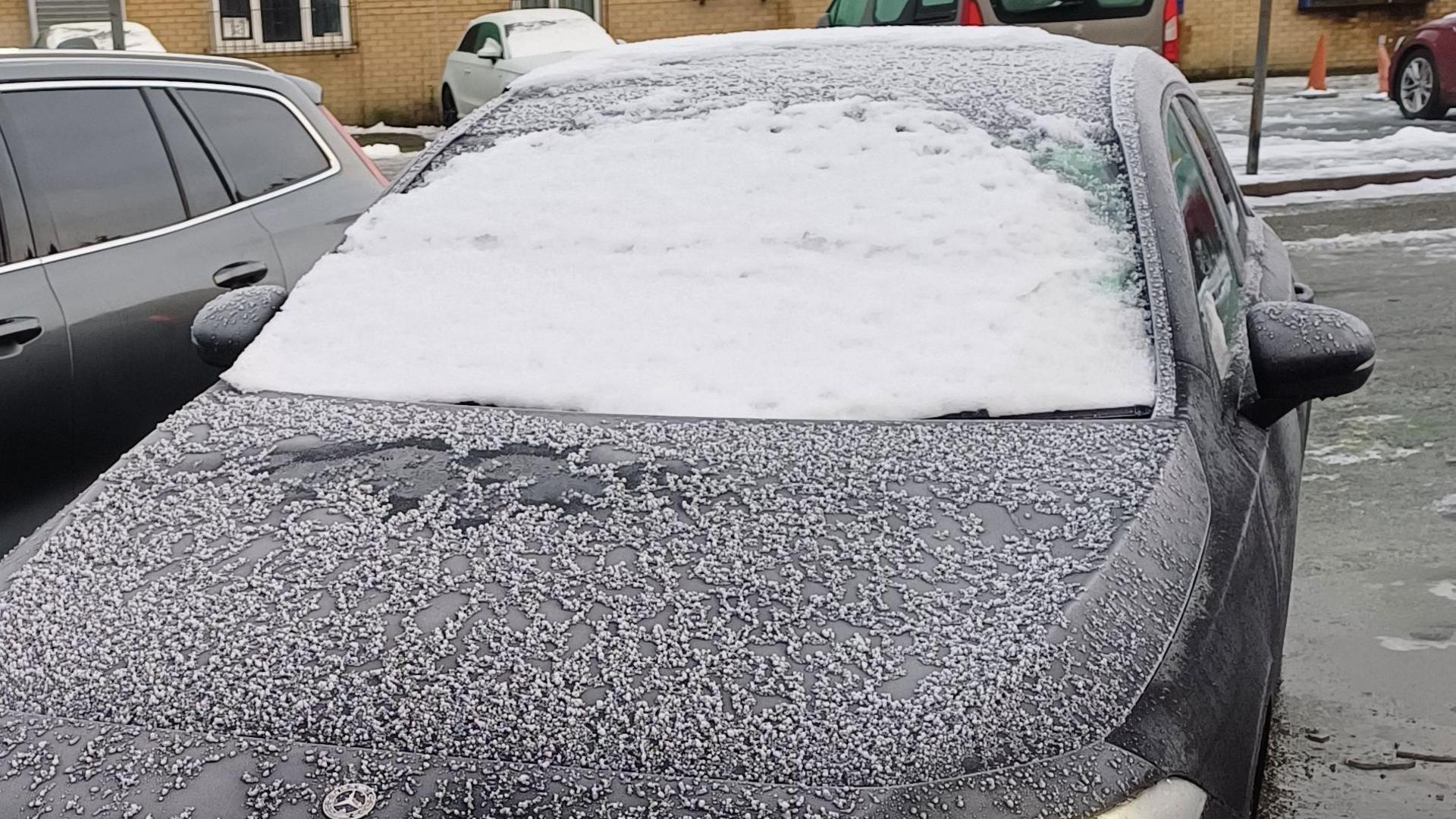 Snow and ice covers the entire front windscreen of a parked black Mercedes car