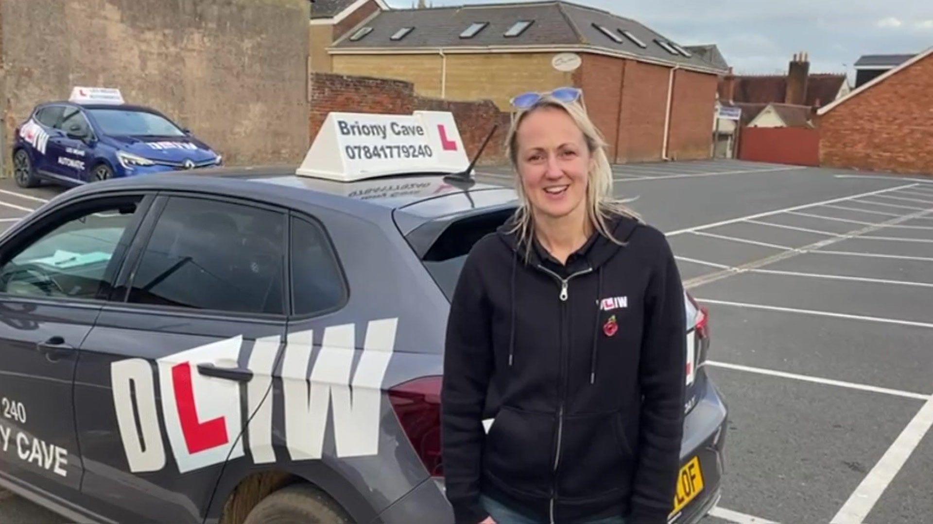 A woman stood in front of a DLIW driving school car