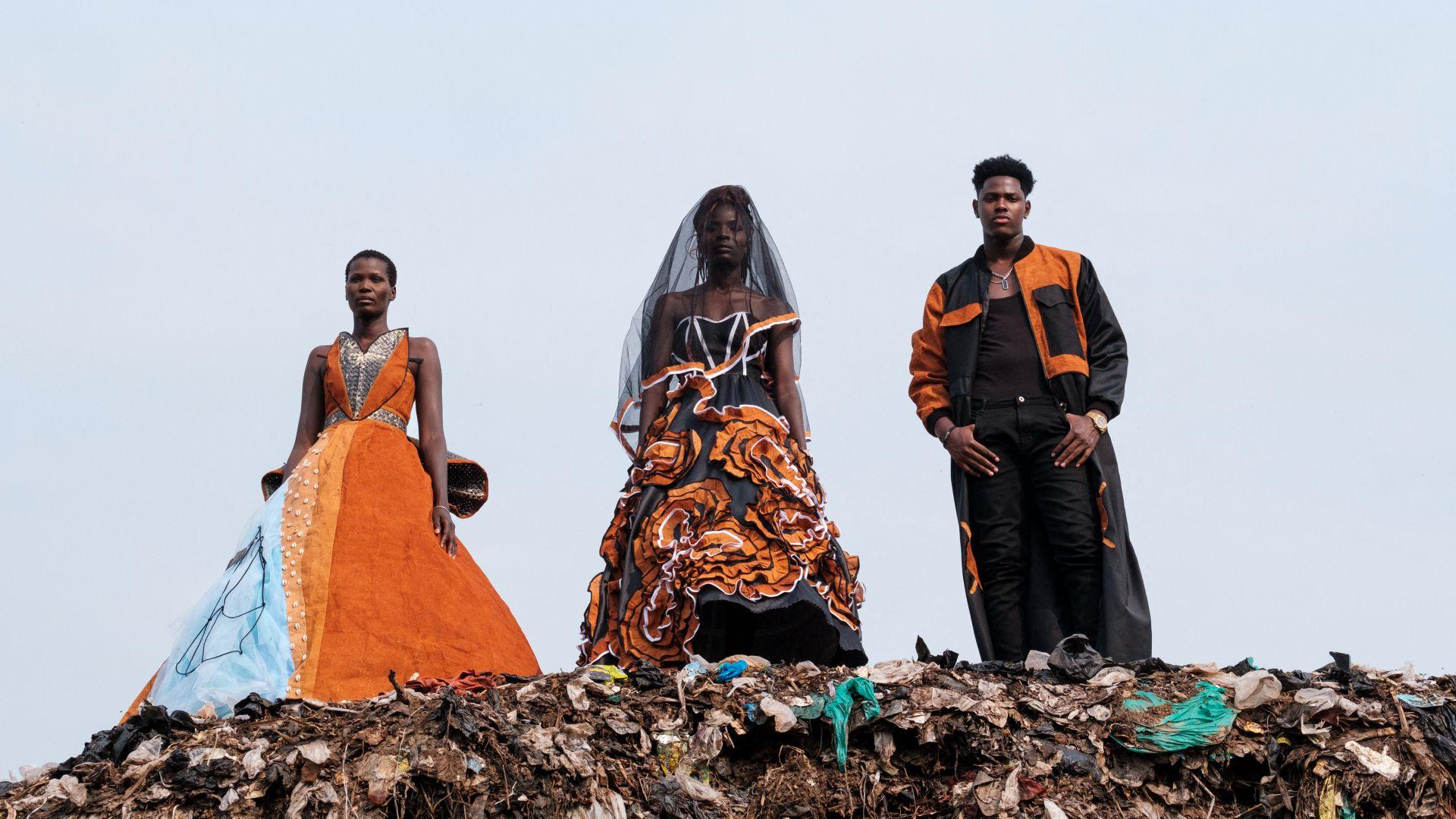 Models wearing black and orange clothes stand on top of a rubbish heap in Kampala, Uganda - Saturday 20 July 2024