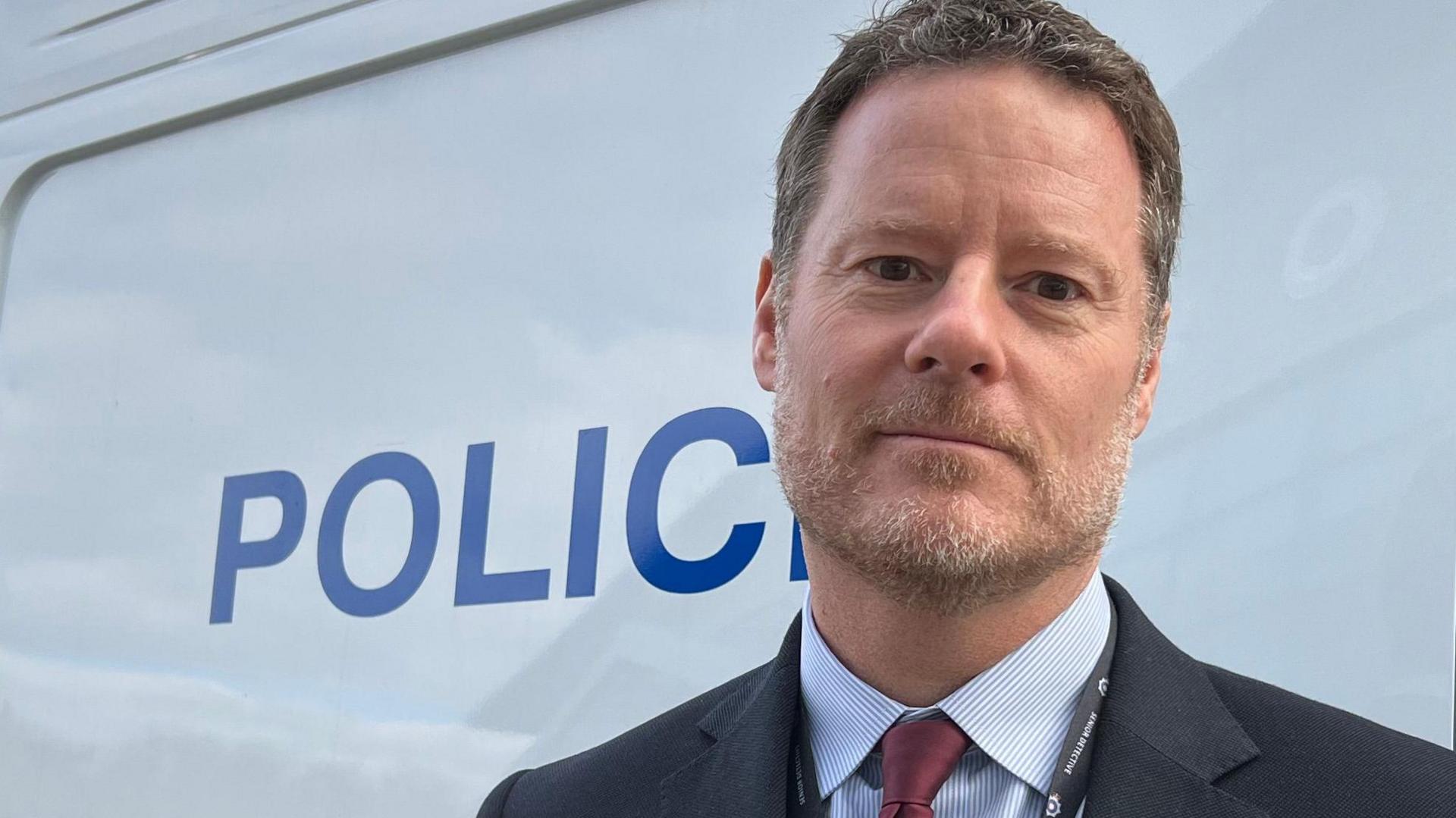 Rich Tompkins in a dark suit with a blue shirt and dark red tie stands in front of a LFR van.