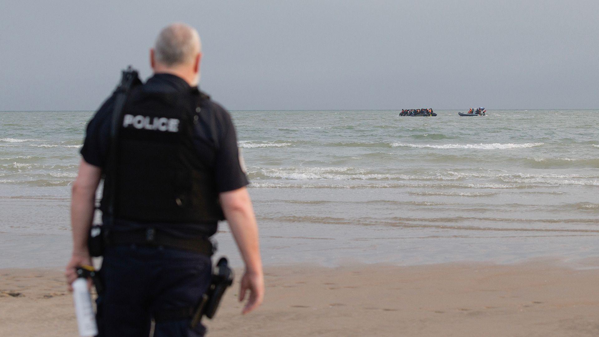A French police officer stands on the beach at Gravelines as a French maritime police rib approaches a small boat off the coast in the background, taken in July.