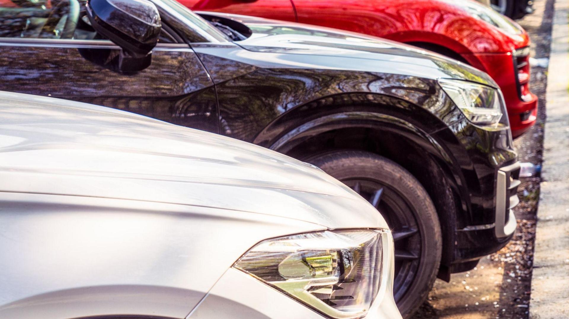 A variety of modern cars, parked with their fronts in towards the curb.