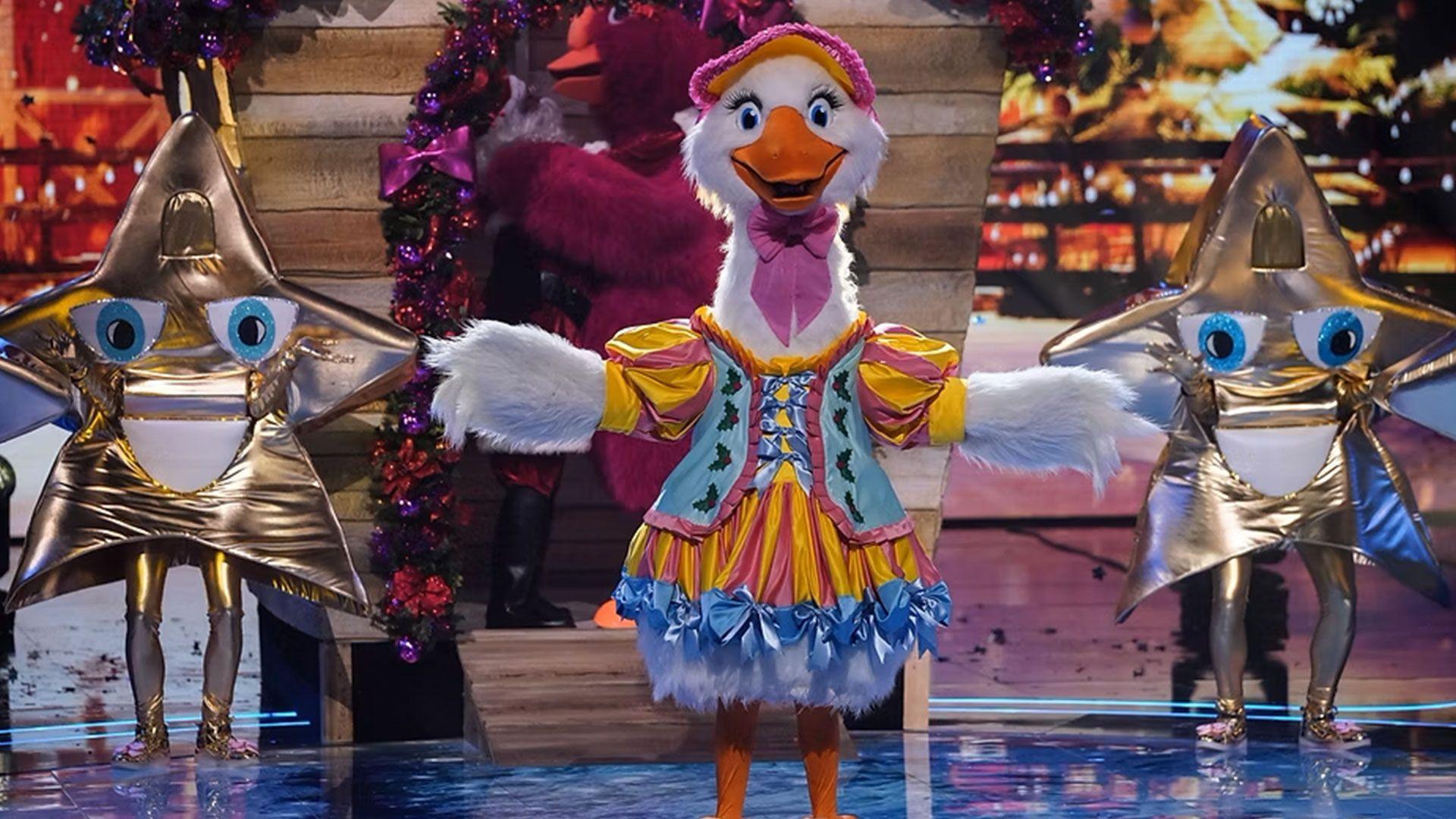A goose costume on the set of TV show the Masked Singer, with people dressed as stars in the background