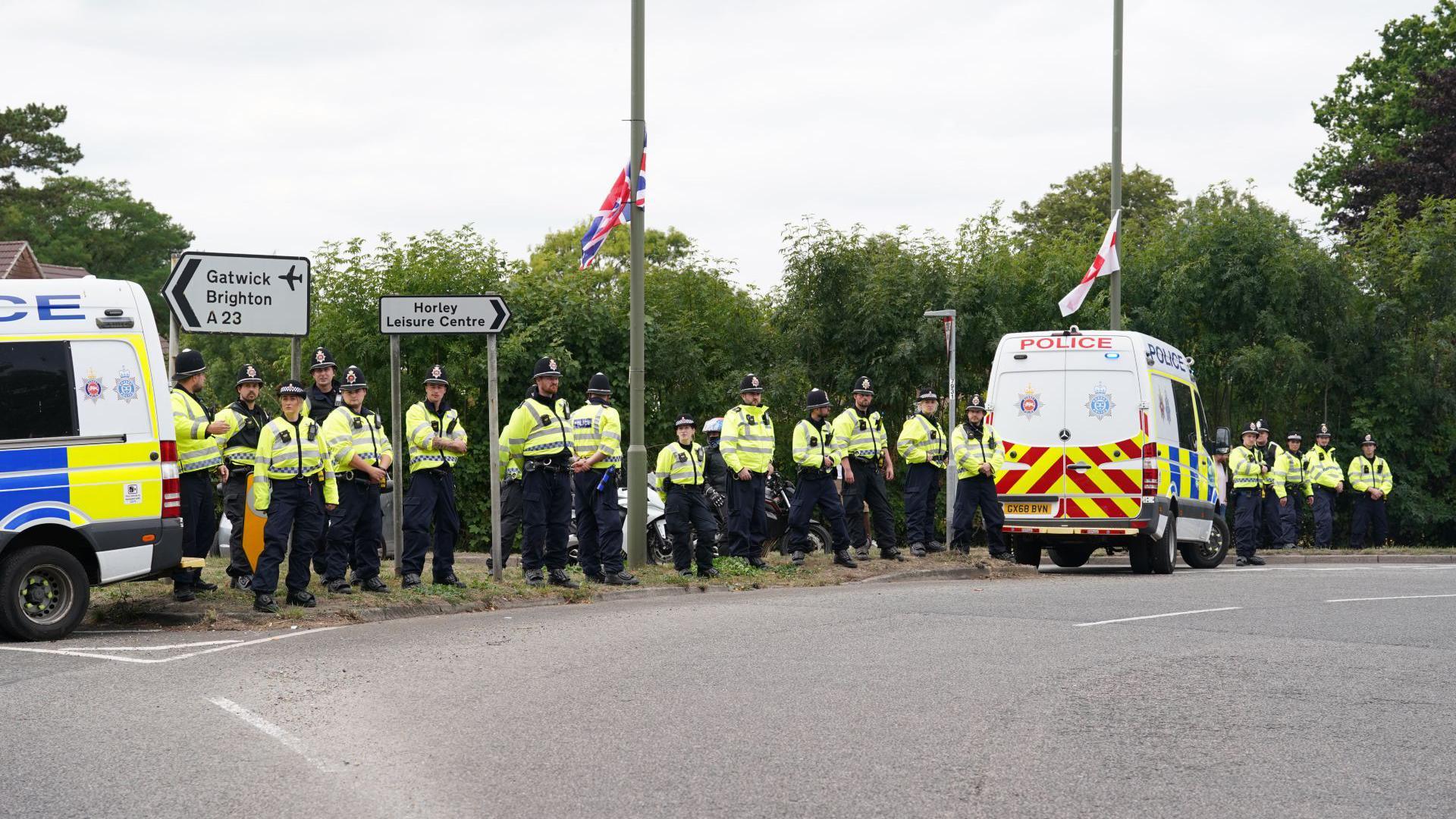 A long line of police officers and vans along a stretch of road.