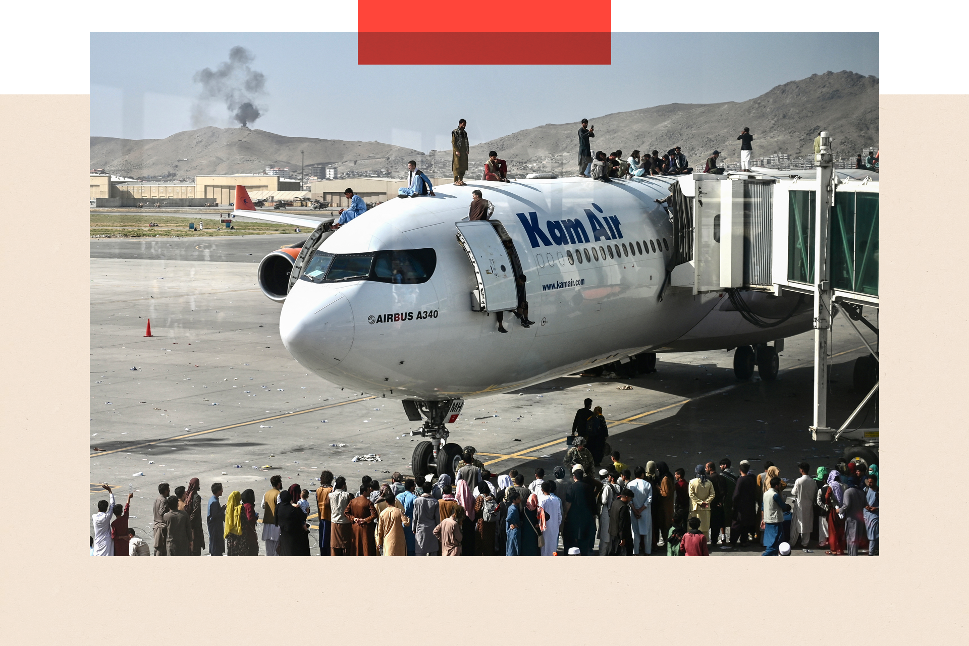 People climb atop a plane as they wait at the Kabul airport, and crowd around, there is smoke in the background