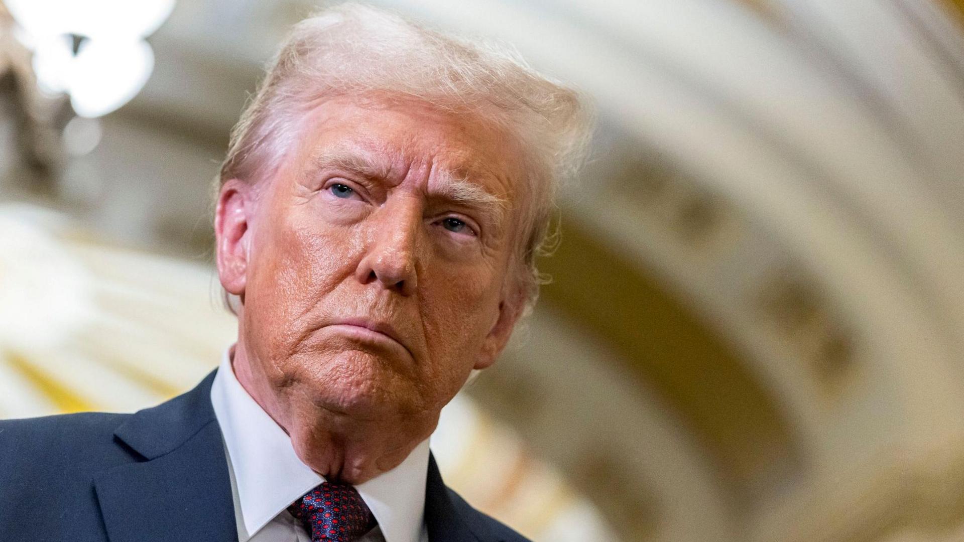 Donald Trump - a close-up image of the president-elect who has short, blonde hair and is wearing a navy suit jacket, a white collared shirt and a blue and red patterned tie.