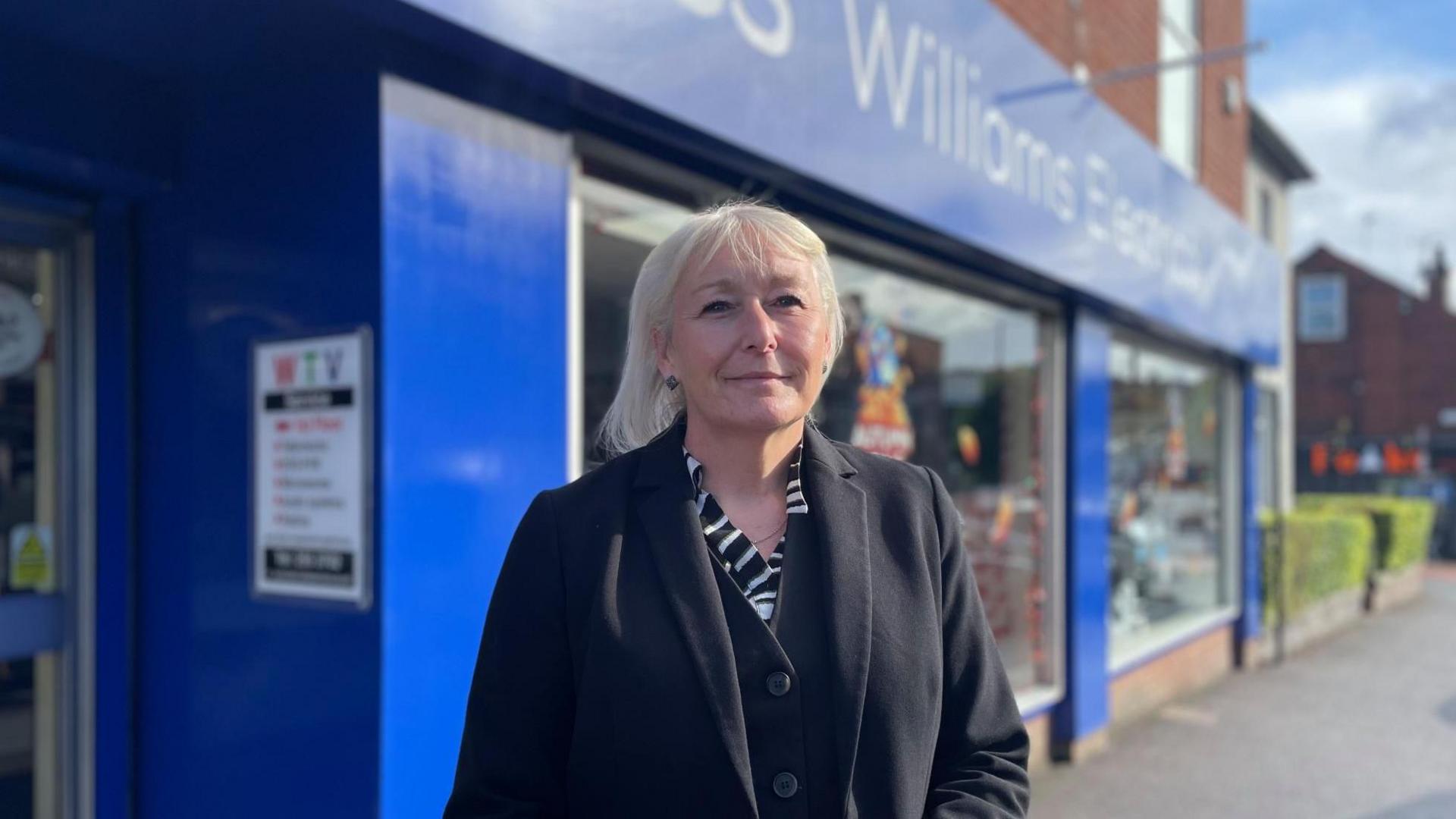 A smartly dressed woman stands in-front of a blue shop front