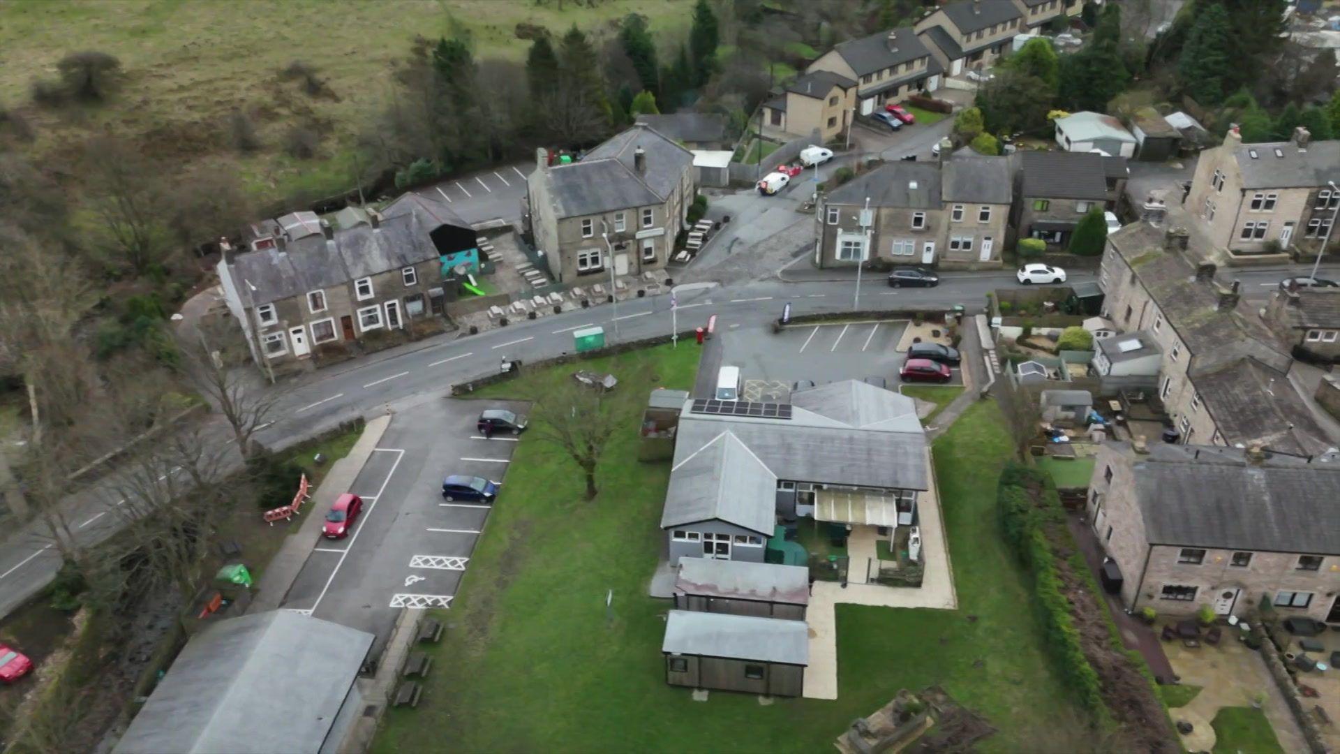 An aerial shot of a village, looking down at a community centre, a pub and housing and a car park, and road