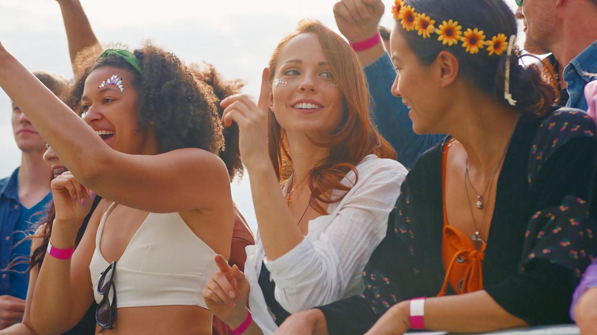 Three women at a music concert wearing colourful clothes, headpieces and make-up