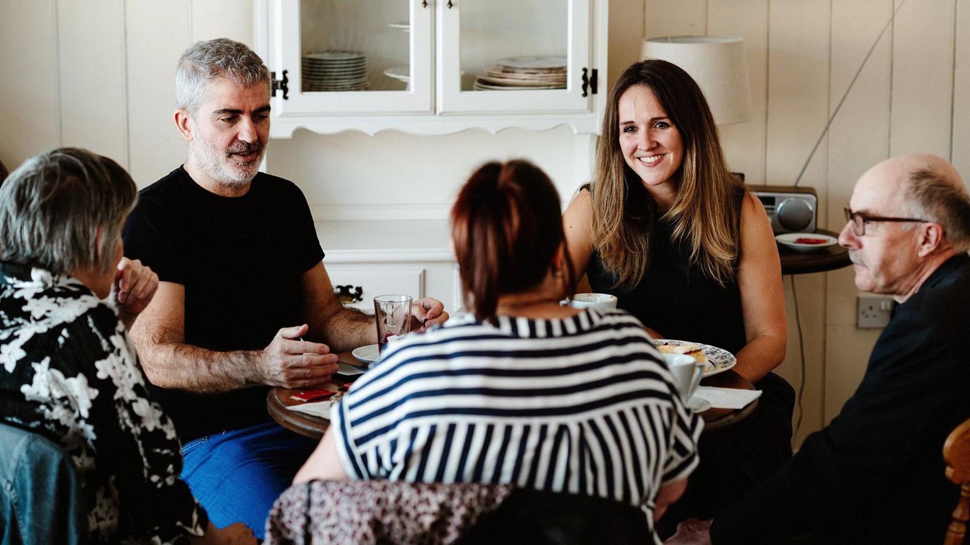 Dr Verena Niyadurupola (right) in a coaching session, with four other people, smiling at them, all sat round a small round table 