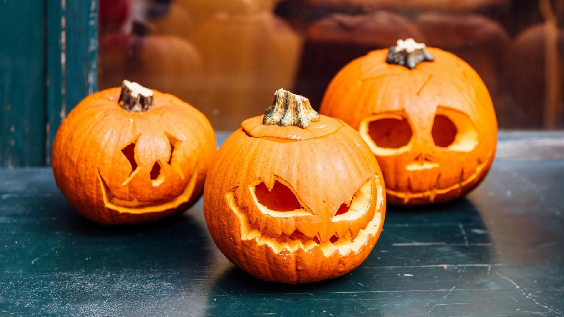 The image shows three pumpkins or jack-o-lanterns with scary faces carved into them 