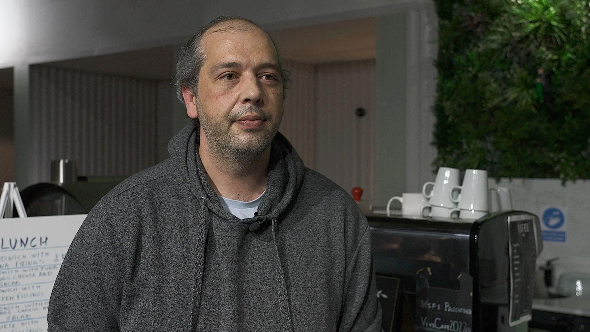 Paulo in front of a coffee machine. He wears a grey hoodie.