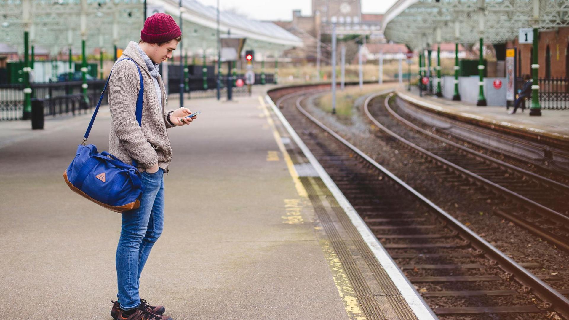 A young man looks down at his mobile phone on the platform of a French train station in an archive photograph