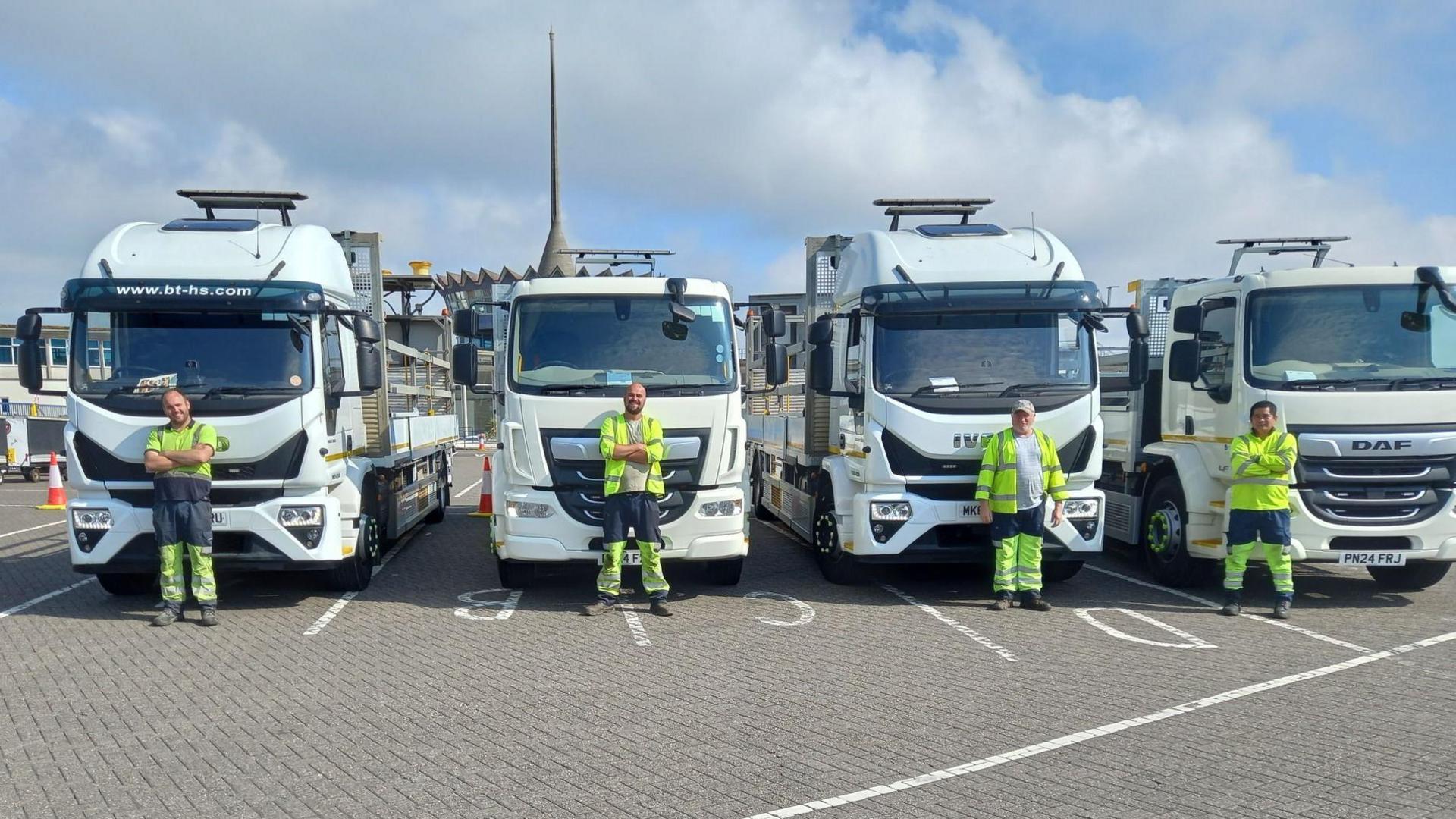 Four large white trucks with drivers stood in front