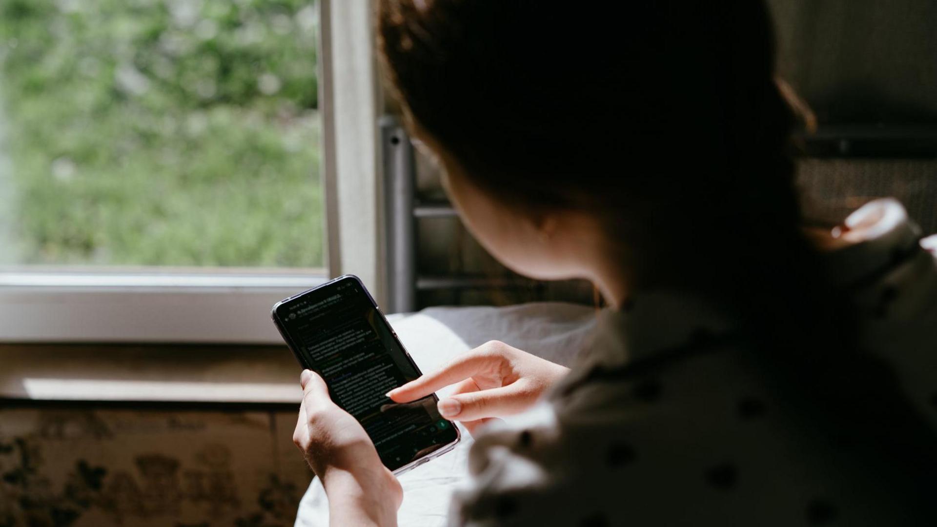 An over the shoulder shot of a young girl scrolling on a phone screen