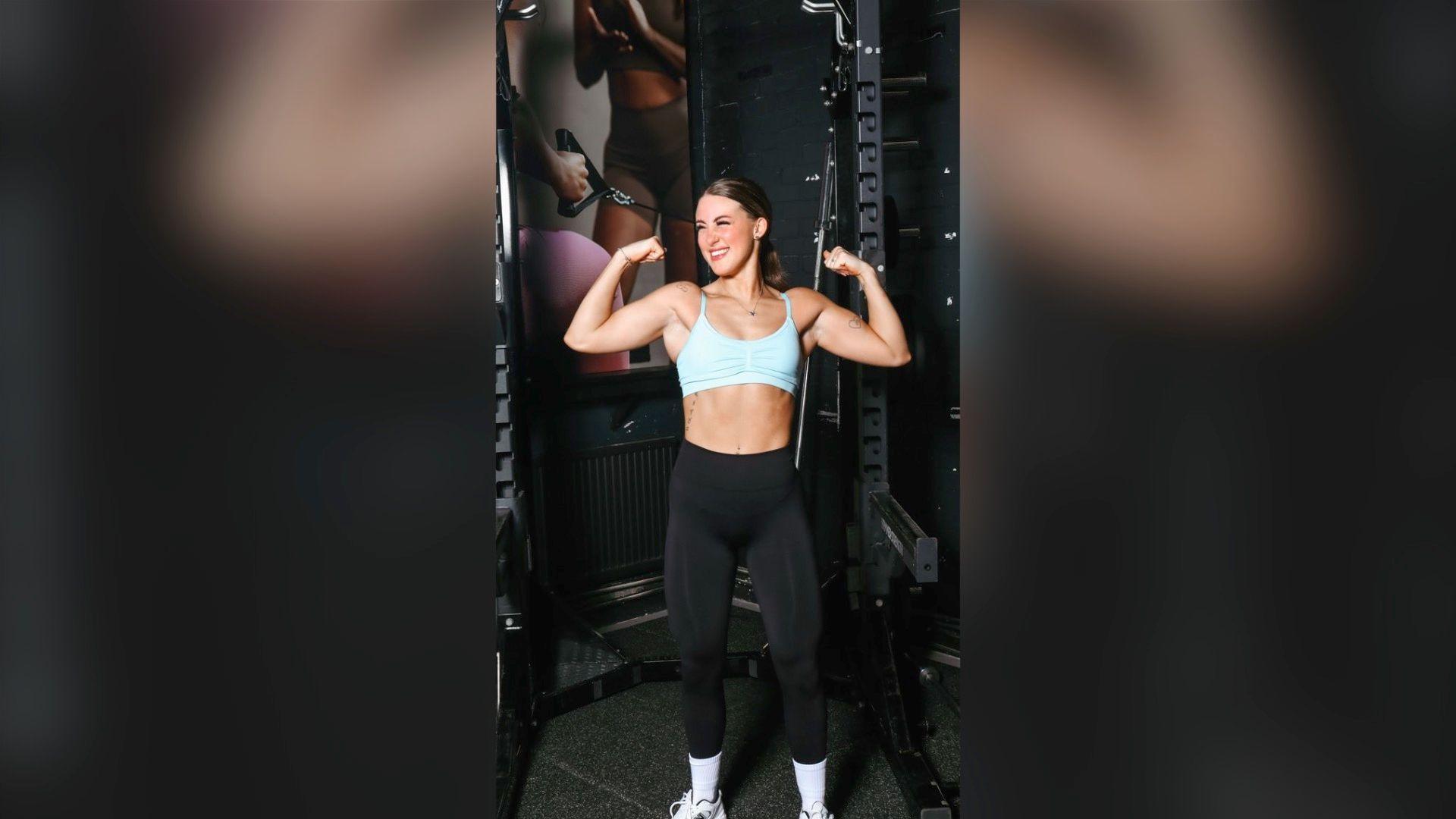 Tia Ainsworth flexing muscles in black leggings and blue sports bra