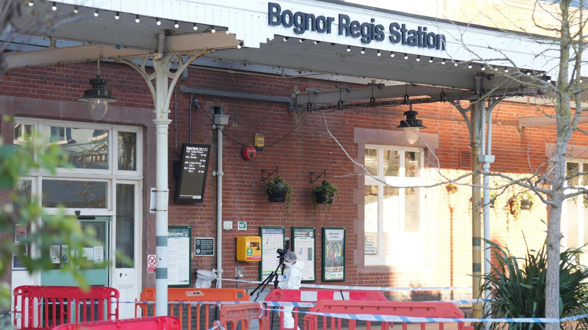 Police tape around a train station in daylight. The area is also cordoned off with red fences. A sign reads Bognor Regis Station.