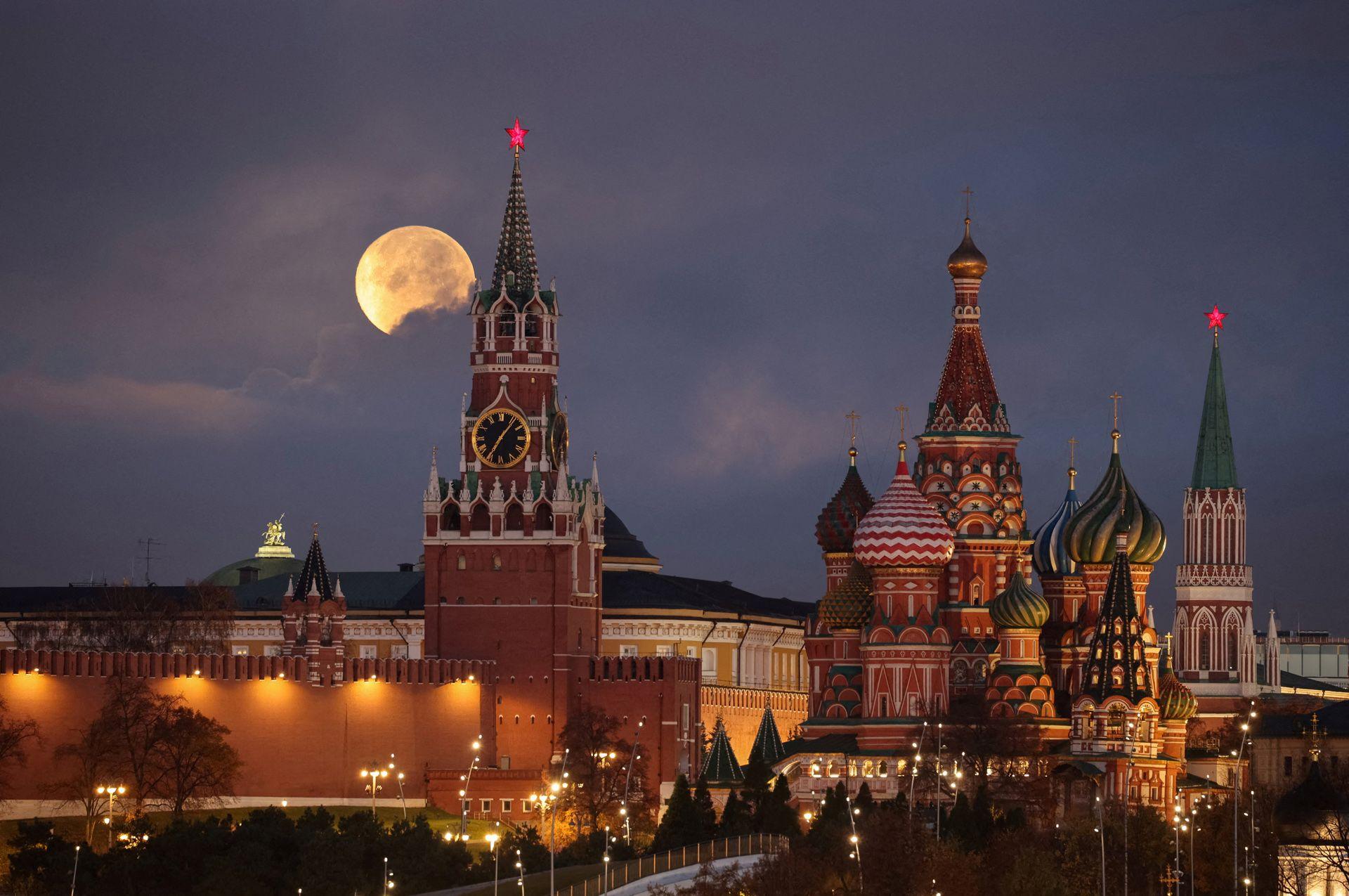 The Moon rises behind pointy Cathedral buildings with architectural detail and streetlights in the foreground in Moscow on Wednesday. The domes and turrets of the cathedral are richly decorated with stripes and zigzags.