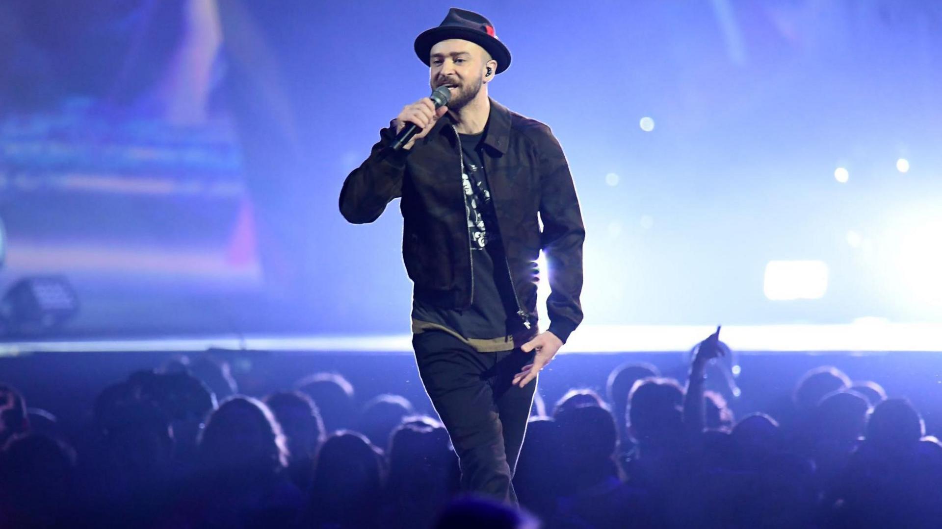 Justin Timberlake performing on stage. He is wearing a black hat, jacket and trousers.