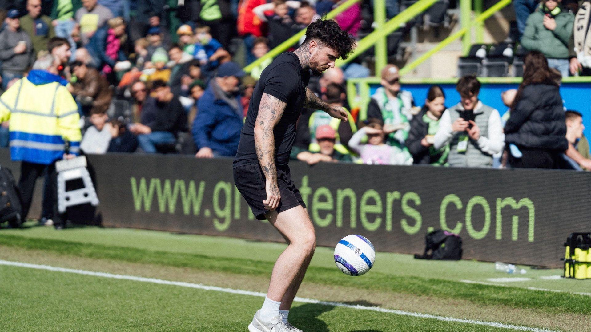 Football fans watching a man with tattoos kicking a white and blue football.