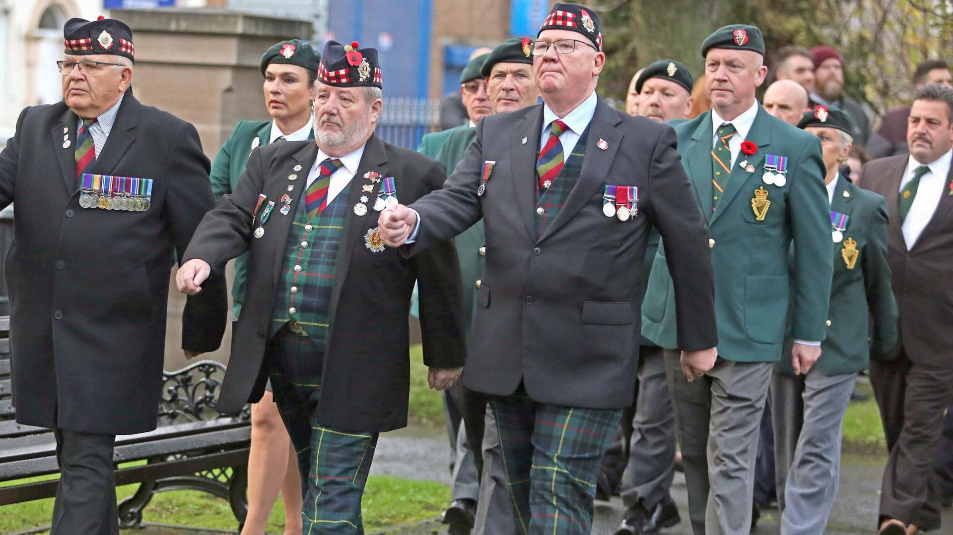 People in green and tartan uniforms wearing medals marching.