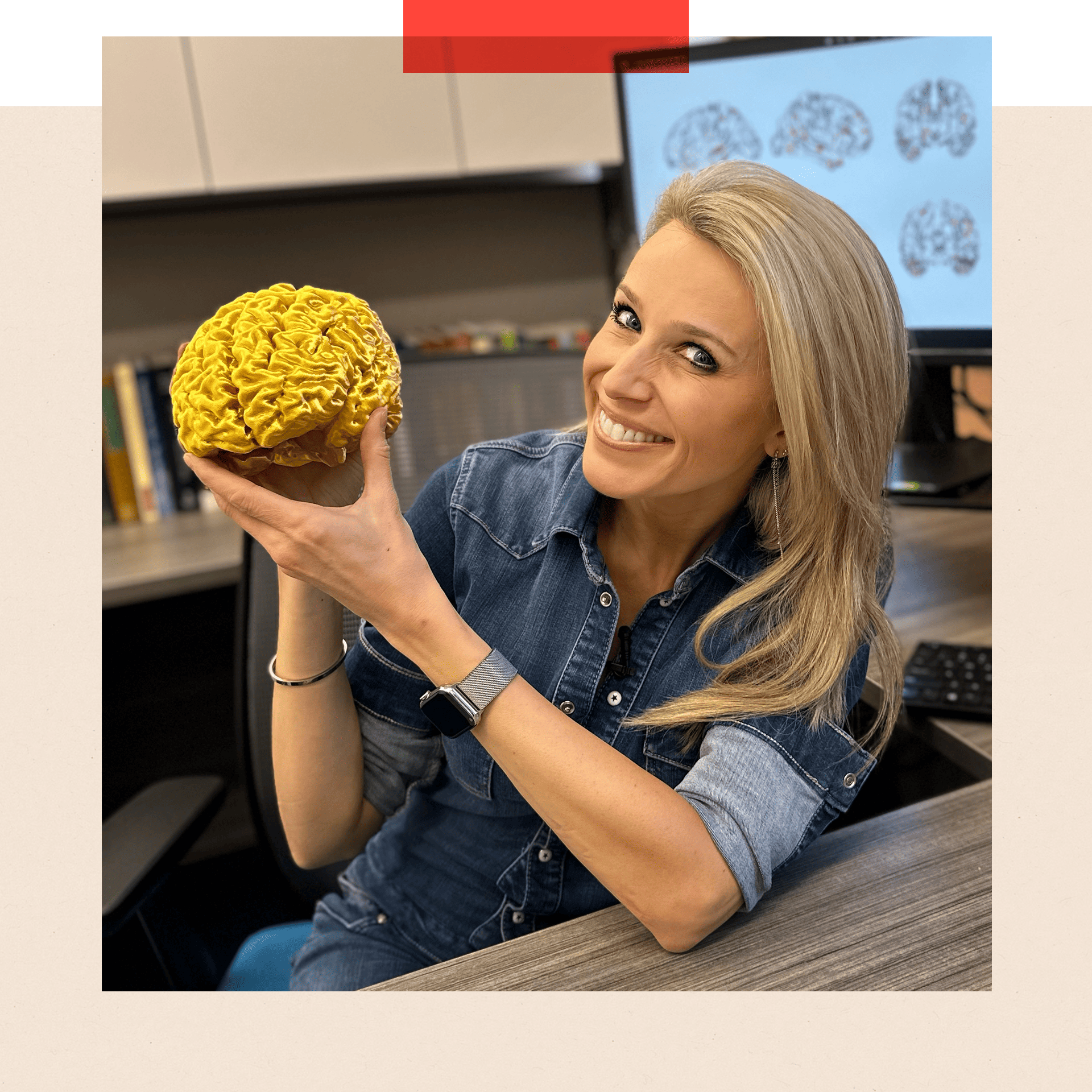 Lara Lewington sitting at table holding a 3D printed gold coloured model of her own brain