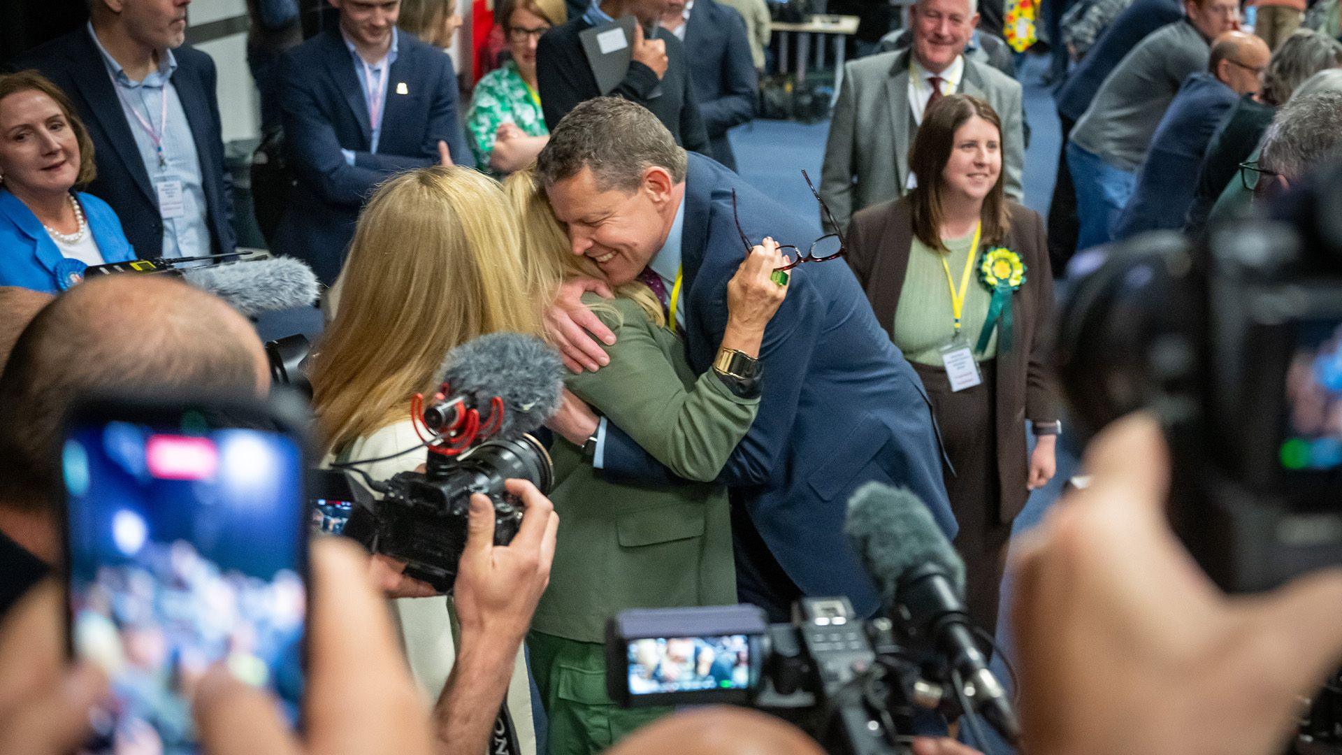 Rhun ap Iorwerth, arweinydd Plaid Cymru, yn cofleidio cefnogwr wrth gyrraedd y ganolfan pleidleisio yn Llandudno