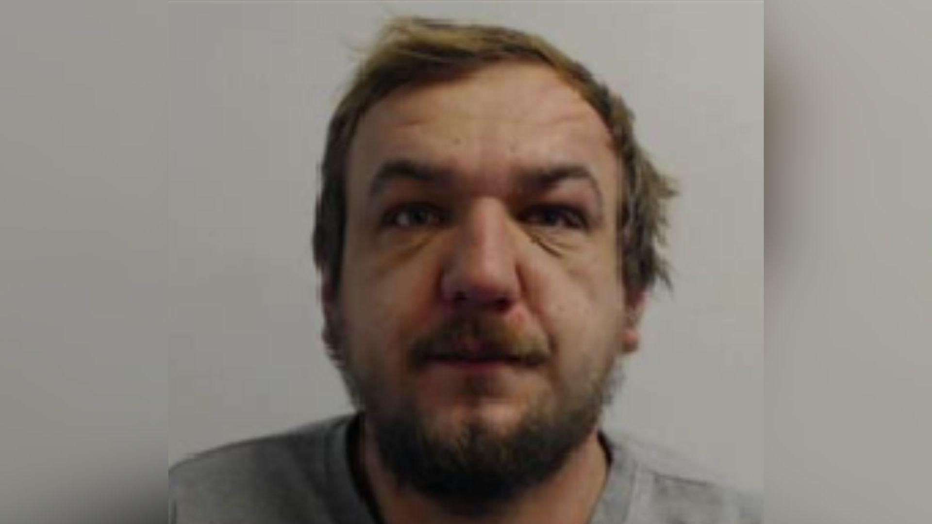 A police mugshot of Mihai Nicolae Patran wearing a grey jumper and standing against a grey background.