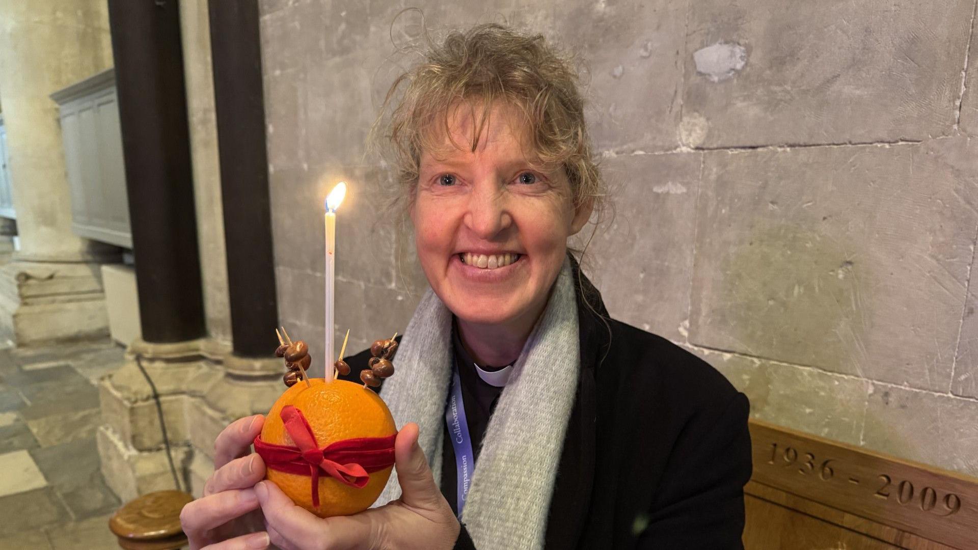 Emma Pennington (a woman with blonde hair holding an orange with a candle coming out of it) with her own Christingle