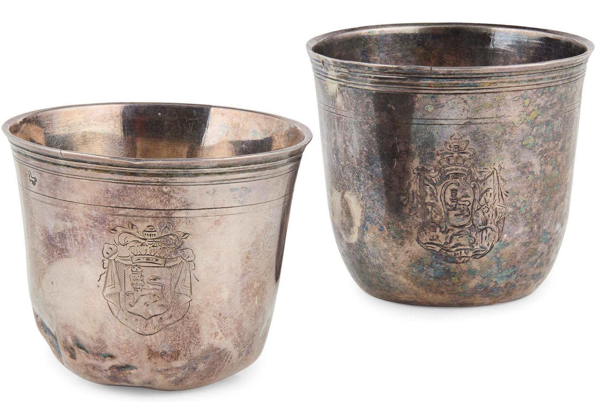 The beakers are cup-shaped and have coats of arms and heraldic crests engraved on the outside.