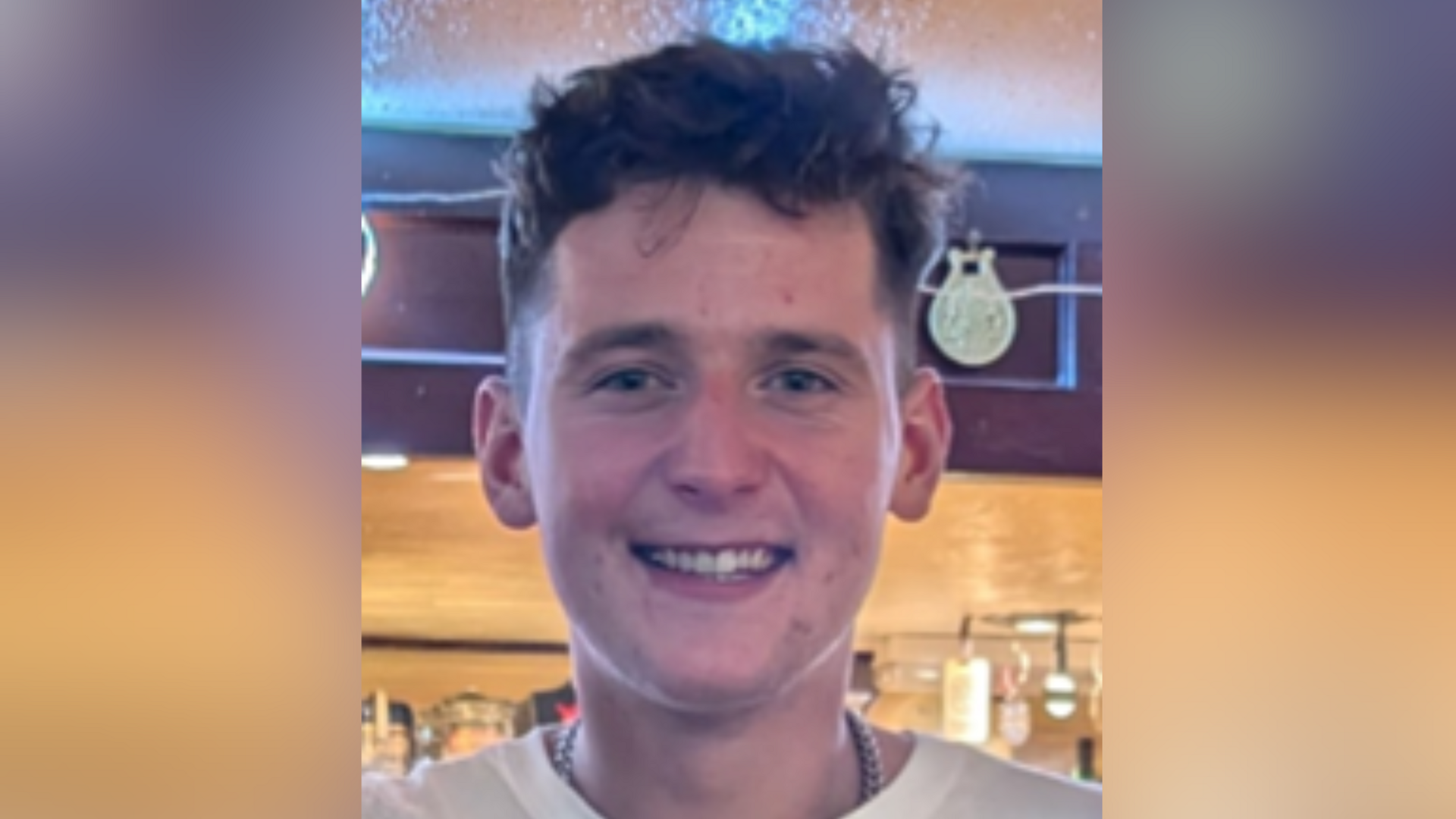Ewan MacDonald smiling straight at the camera. He has dark hair and is wearing a white T-shirt.