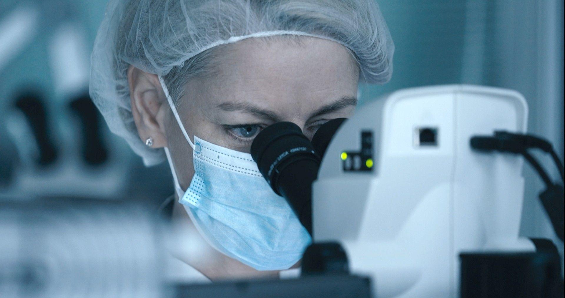 Close up of senior forensic scientist Joanne Cochrane examining an item through a microscope in a lab at the Scottish Crime Campus. She is wearing a face mask and a hair net to prevent contamination. 