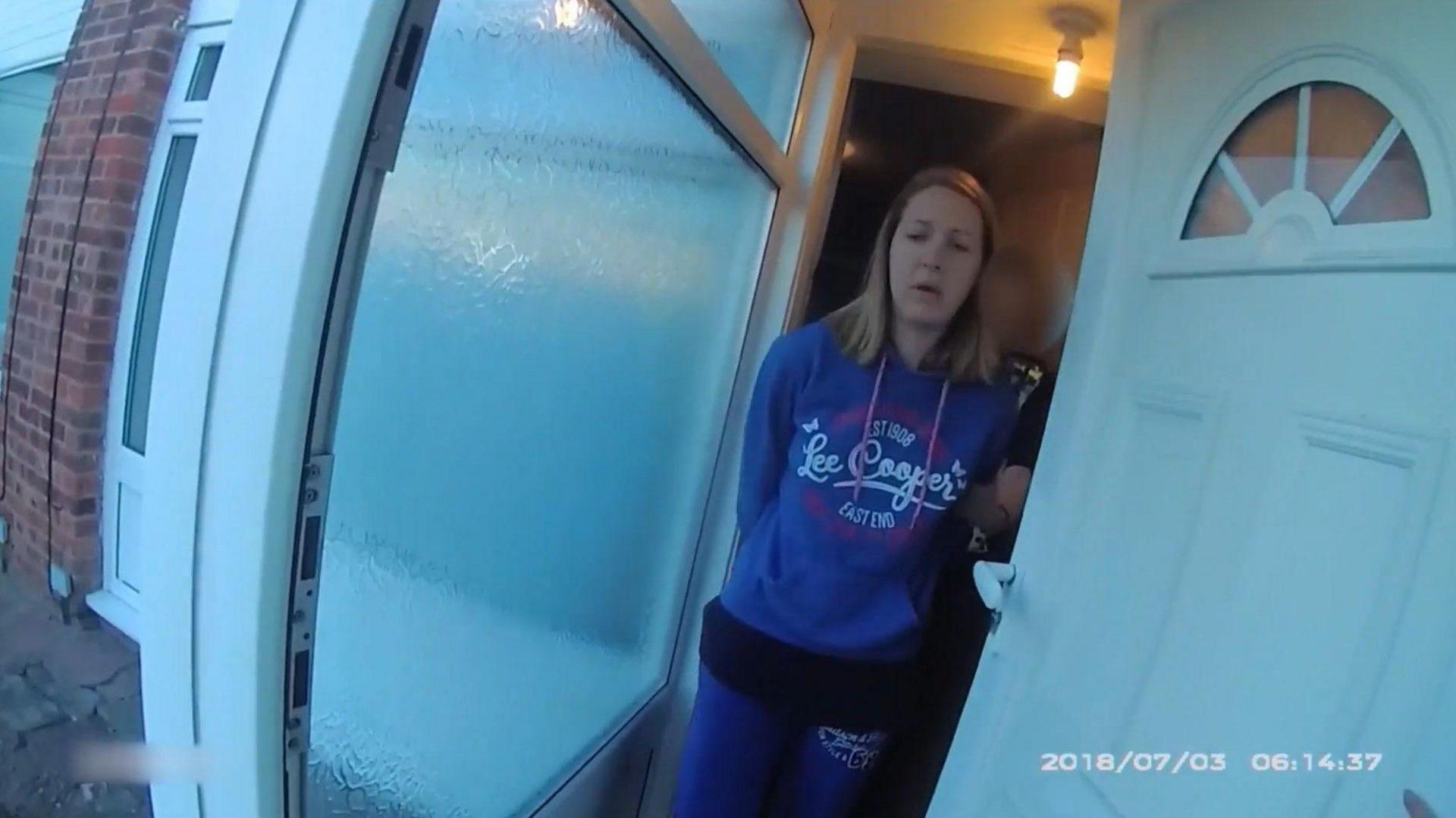 Lucy Letby being arrested at her home, emerging from the front door in handcuffs and dressed in a blue hoodie