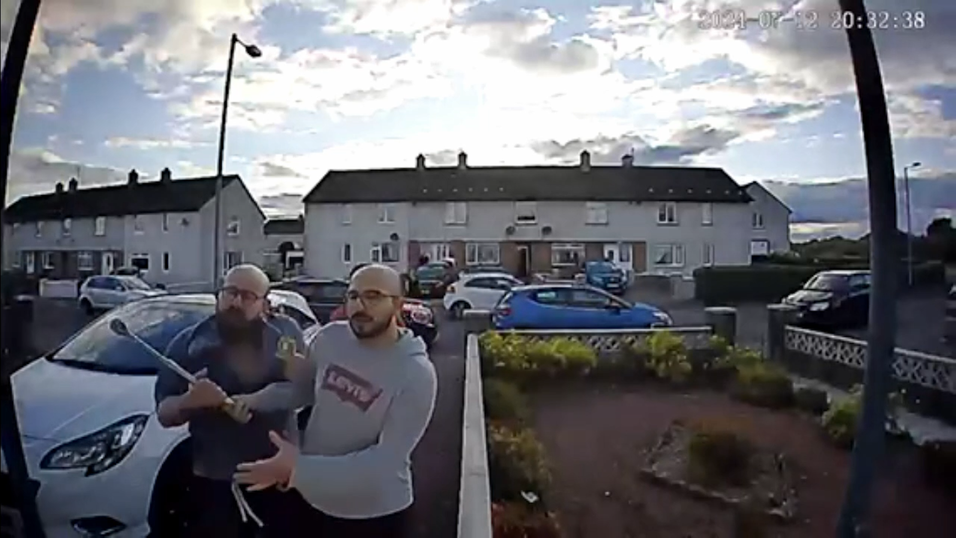 Doorbell camera footage showing two bald men, both with glasses and beards. They both have their hands on some kind of metal pole. 