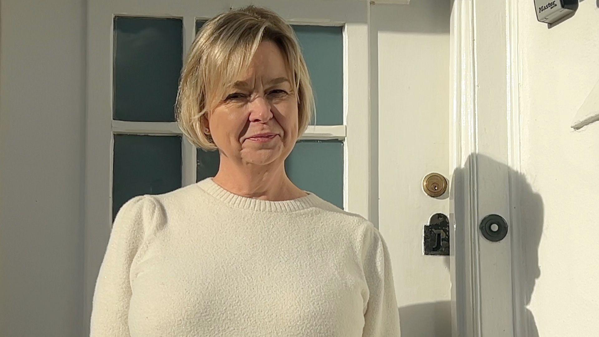 Lucy Green has short blonde hair. She wears a cream coloured jumper and stands in front of a door.