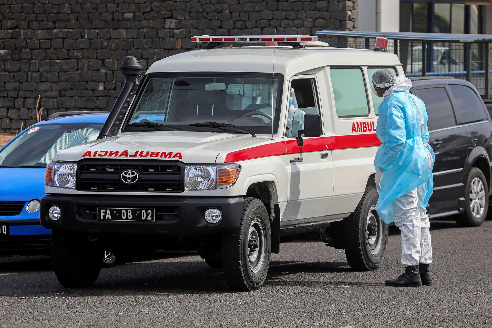 A truck-style ambulance is stopped on a street while a person in a hazmat suit stands next to it talking to the driver, also in a hazmat suit, as they evacuate a person from the ship to the airport to be transferred to the Netherlands for treatment, in Cape Verde on Wednesday.