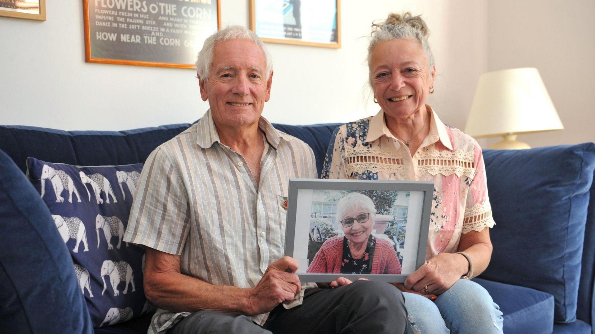 Two family members - Paul Fry and Amanda Gaunt - sit on a navy blue sofa clutching a picture of Adrienne Fry, who donated her organs after dying of a brain haemorrhage. 