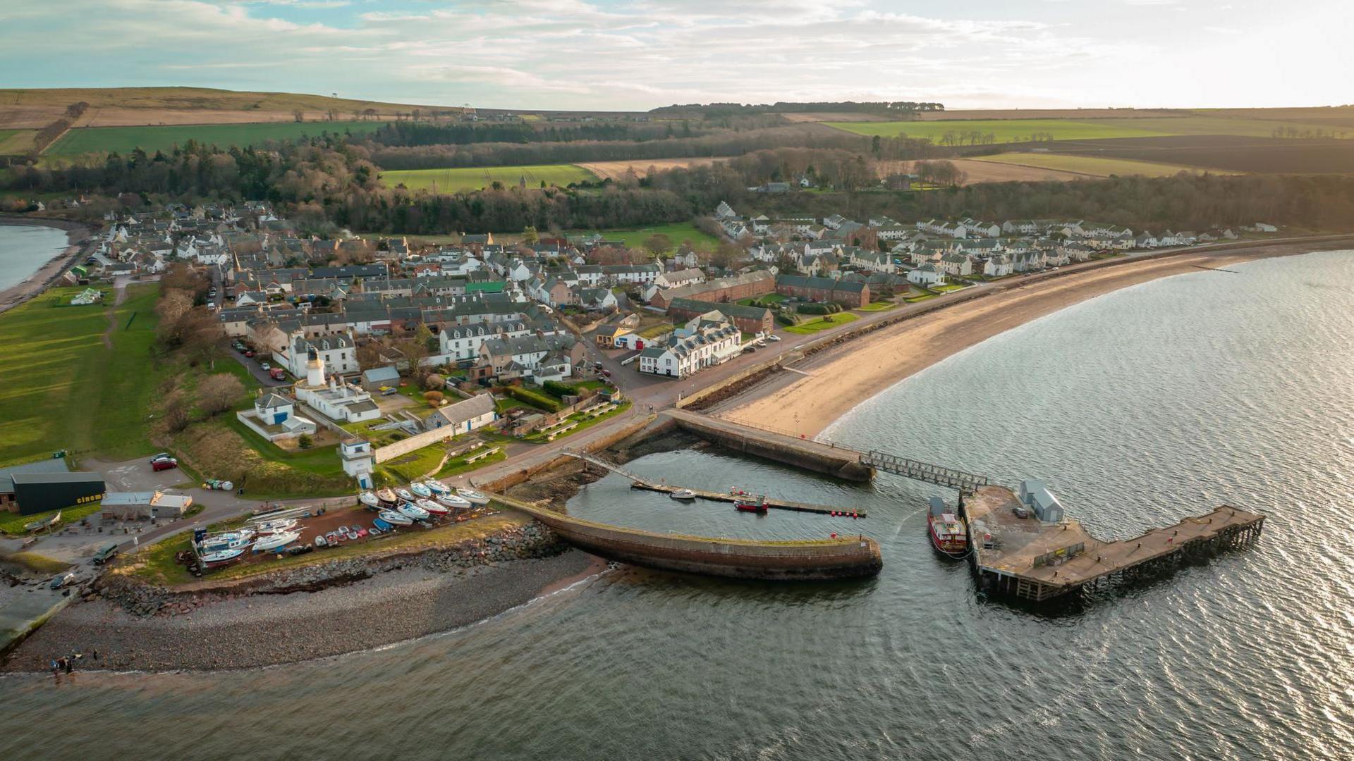 An aerial view of the village showing its rows of white-walled houses and its harbour. There are boats hauled up on the shore.