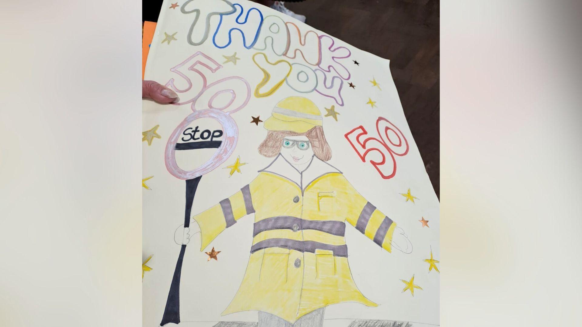 A handmade card. It says "thank you" with the number 50 written around it all in bubble writing. There is a pencil drawing of Jackie in a neon yellow jacket holding a stop sign.