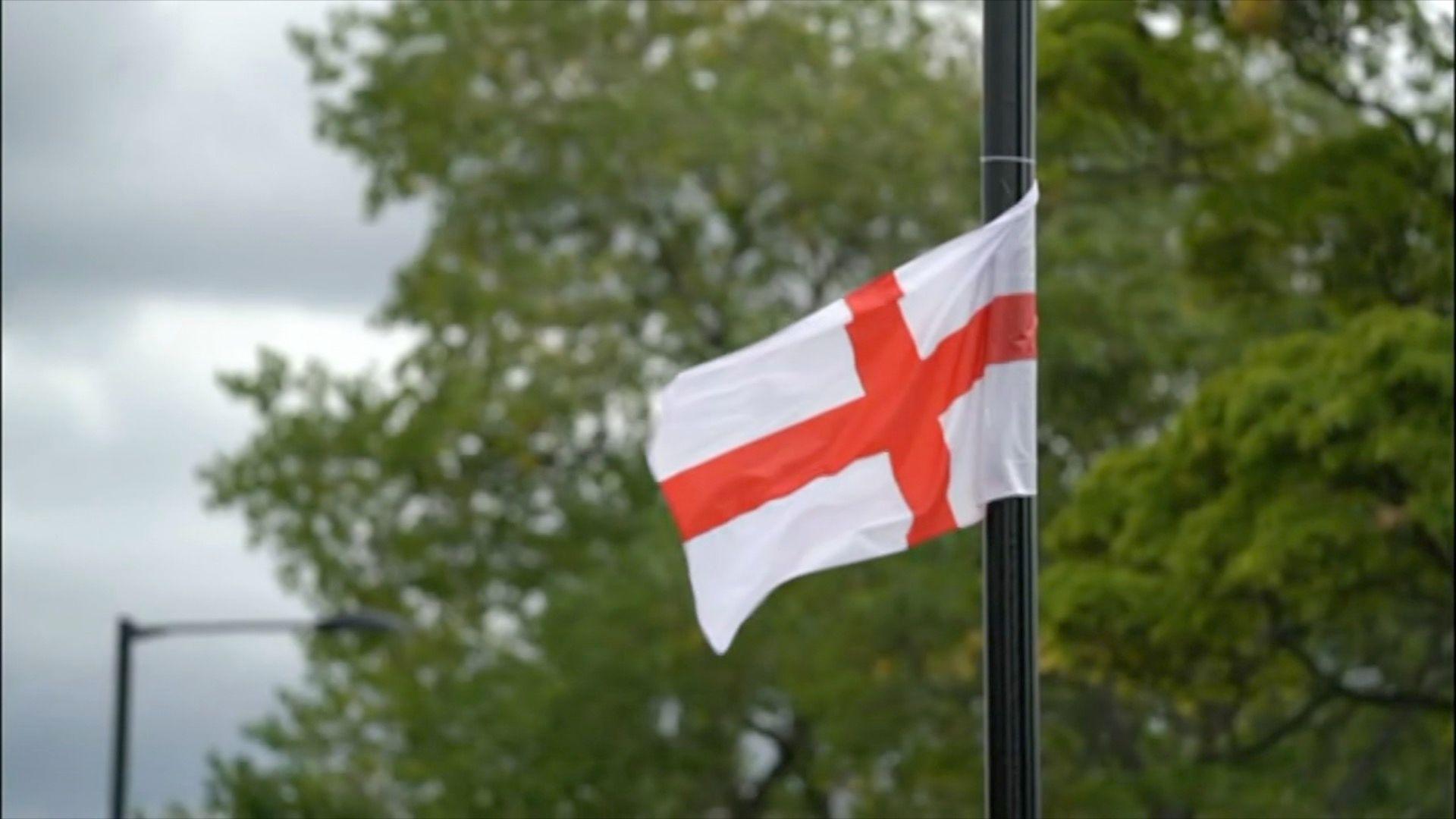 A St George's flag flies from near the top of a black lamppost in Birmingham. It is attached to the pole with cable ties and is seen fluttering in the breeze.
