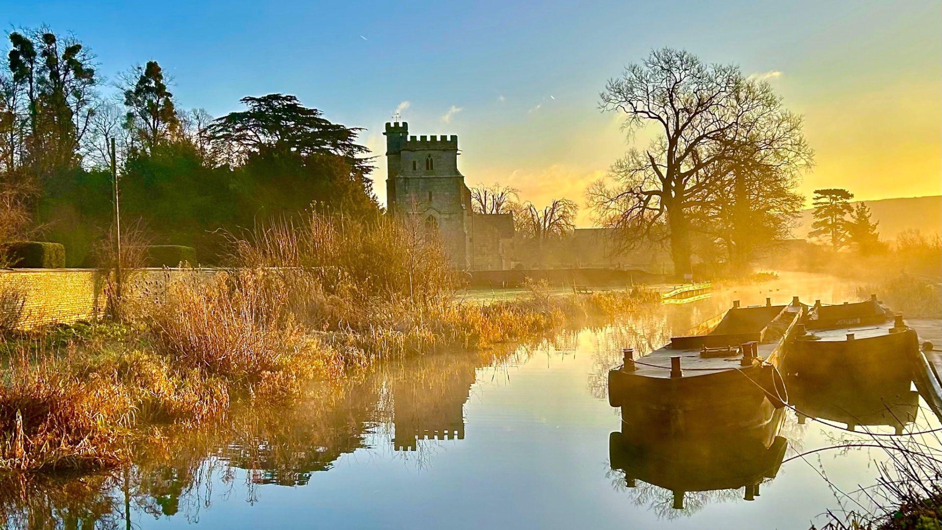 Misty canal photography with some wooden boats and a castle in the background.