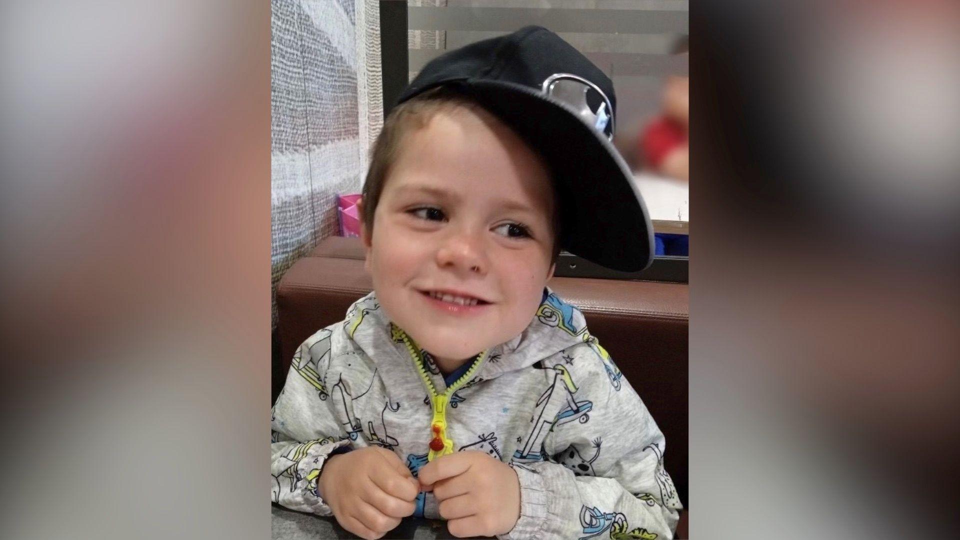 A little boy with a baseball hat, grey hoody and yellow zip up top.