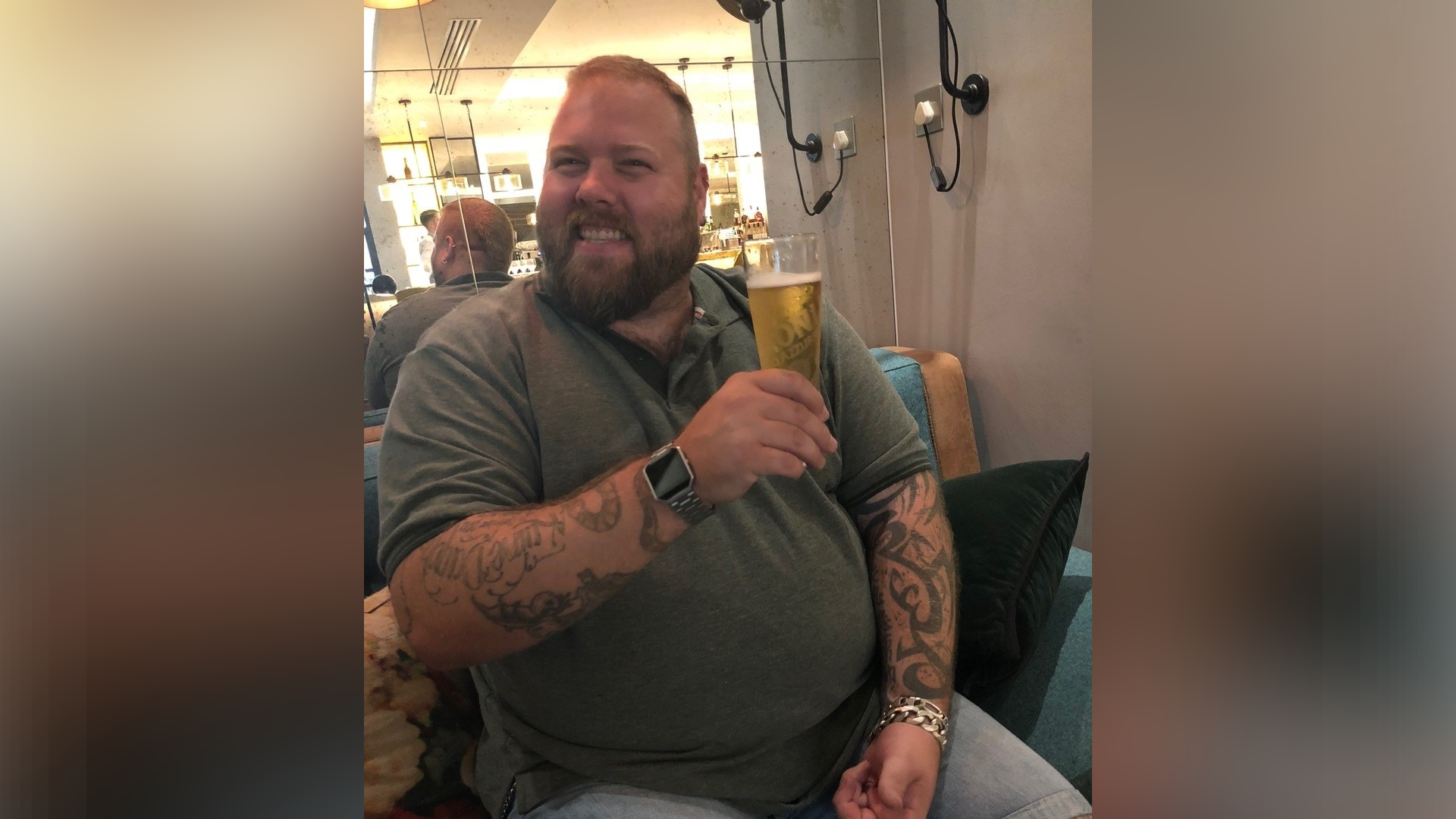 Mr Hammond smiles as he holds a pint of beer in one hand. He wears a green top with blue jeans.