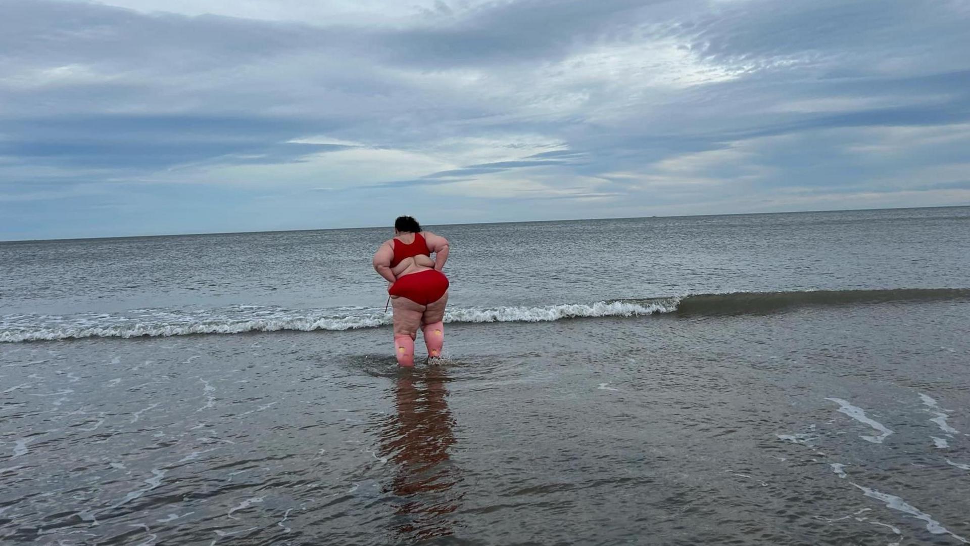 Katie standing in the sea facing away from the camera. She's wearing the same red bikini as in the animation.