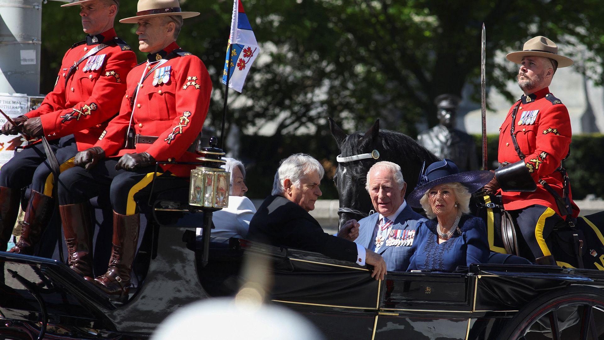 King Charles and Queen Camilla sit in a black carriage.
