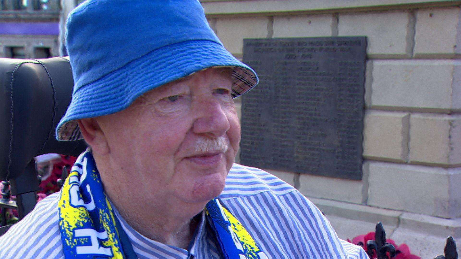 Ken Harker. He has a white moustache, wearing a blue bucket hat, blue and white striped shirt and Dungannon scarf.