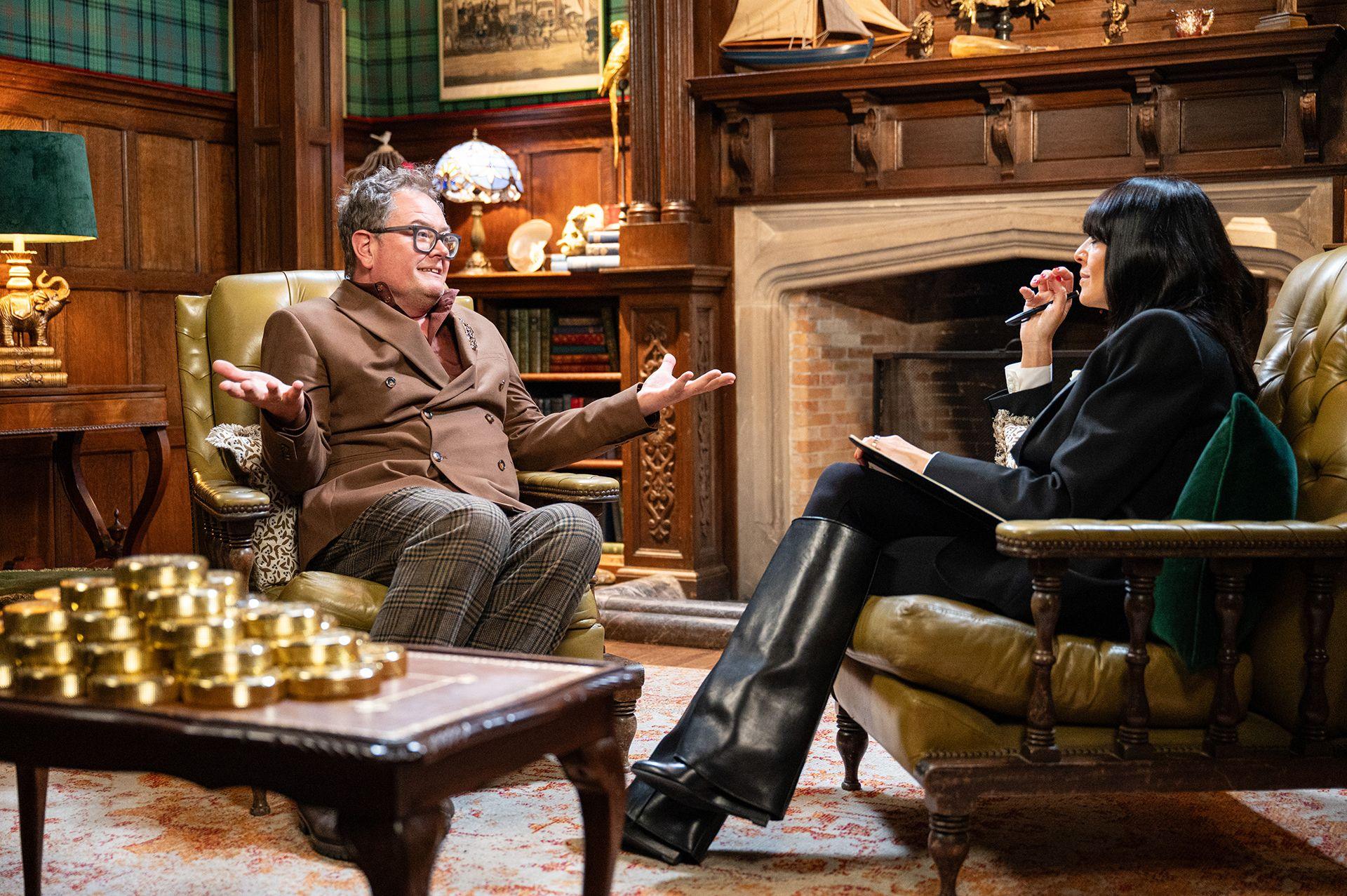 Alan Carr, sitting in an armchair, speaking to Claudia Winkleman on the Celebrity Traitors
